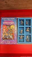 Seven distinct silver metal robot miniatures arranged in blue foam insert inside original box, numbered in red on bottom.