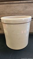 Front view of beige stoneware crock showing cylindrical shape and flared rim with minor chip on rim.