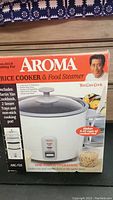 Front of the box showing Aroma Rice Cooker & Food Steamer with image of the cooker, Martin Yan cookbook included, and branding.