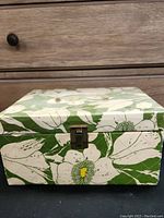 Closed view of the green floral patterned box with white flowers and metal latch.
