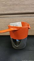 Orange Copco cast iron sauce warmer with handle on metal base with burner, includes original instruction booklet visible inside pot.