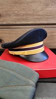 Navy blue vintage Flight Ace pilot hat and partial view of olive green hat on red box with wooden background.