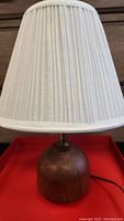 Front view of the lamp showing the teak wood rounded base and pleated white fabric lampshade.