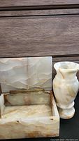 Open rectangular onyx stone box with natural earth-tone veining and hinged lid next to matching vase.