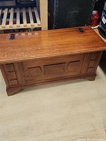 Front view of vintage wooden chest showing carved front panel and lid with metal hinges.