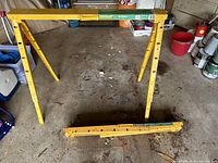 Two yellow adjustable height metal sawhorses shown; one open and standing, one folded flat on the ground for storage.