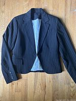 Black pinstripe blazer with light lining laid flat on wooden floor