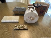 Four vintage purses shown together on table: white pearlescent shell purse, white clutch, metal basket weave purse with lucite lid and handle, wooden cat-shaped purse.
