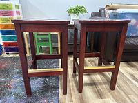 Rear view of two cherry wood bar stools showing square legs and brass footrests