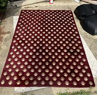 Full view of the dark red wool rug laid outdoors showing the beige leaf/paw pattern across the entire surface.