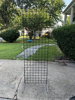 Full view of the black metal grid display rack standing outdoors on concrete with grass and walkway in background.