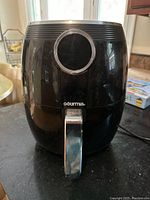 Black Gourmia air fryer on kitchen counter, showing front handle, brand logo, and control dial.