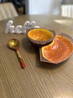 Photo showing a painted wooden Russian spoon, 1970s orange/brown bowl and dish, and a white marble "hello" decorative piece on a wooden table.