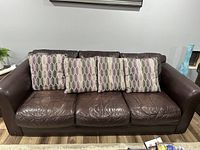 Front view of the leather couch with four decorative pillows on it.
