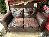 Front view of the brown leather loveseat couch showing two seat cushions and two back cushions with visible wear on one seat cushion.