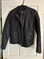 Front view of black leather jacket with quilted shoulder and chest details, zippered pockets, and snap collar.