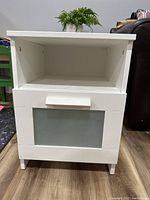 Front view of the table showing drawer with frosted glass panel and handle, open shelf above, standing on floor.