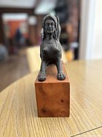 Front view of antique metal sphinx sculpture showing detailed human face and front paws on wooden base