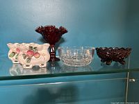 Five candy dishes including a clear crystal bowl, deep red and dark purple glass dishes, and two white porcelain dishes with apple design.