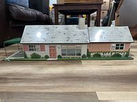 Front view of the metal dollhouse showing exterior details including the roof, chimney, windows, door, and landscaping.