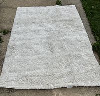 White shag rug laid out on pavement showing overall size and condition