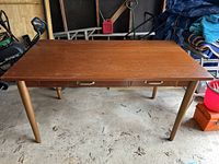 Solid wood desk with smooth medium brown finish, shown from the front on a concrete floor.