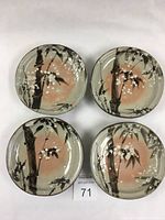 Top view of the four Japanese hand thrown ceramic plates, showing detailed brushwork decoration of bamboo and white blossoms on a greenish glaze with peach center.