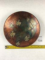 Top-down view of circular raku pottery bowl showing leaf design and color variation.