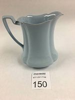 Front-side view of light blue ceramic pitcher showing ribbed body and scalloped rim with platinum trim.