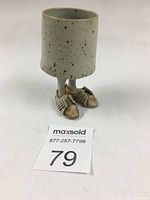 Front view of a handmade small ceramic cup with sculpted legs and shoes showing distinct shoe details.