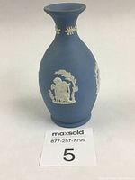 Full front view of the blue Wedgwood jasperware bud vase showing white cherub reliefs and matte finish.