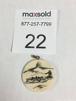 Front view of round faux ivory pendant showing detailed scrimshaw of sled, huskies, and driver with landscape background.