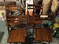 Four wooden folding chairs viewed from front and side, showing seats and backs. One chair clearly has a taped "Guest Chair" sign on top backrest.