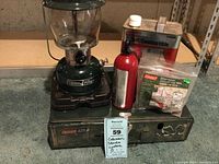 Photo of Coleman Powerhouse two mantel lantern, metal Coleman liquid fuel can, red fuel bottle, fuel filter, and Coleman two burner stove Model 425.