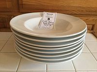 Eight stacked white pasta bowls showing the side profile and depth in a well lit setting on a tiled countertop.