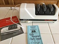 Front view of Chef's Choice EdgeSelect 120 electric knife sharpener with power cord and instruction booklet on tile surface.