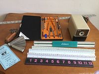 View of partial Alvin drafting set, multiple rulers, thickness gauge and Boston electric pencil sharpener arranged on table.
