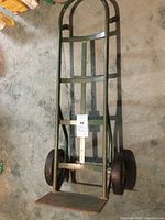 Top view of green metal two wheel hand truck showing the frame, wheels, and base plate against carpeted floor.