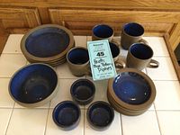 View of full set showing plates, bowls, mugs and small dishes with blue glaze interior and tan rims and exterior.