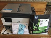 Front view of the HP OfficeJet Pro 9010 printer with power cord, printer manuals, and box of new HP 962XL Dual Black XL cartridges