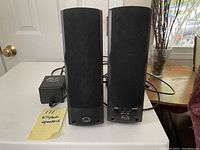 Front view of pair of black Klipsch ProMedia Ultra 2.0 speakers with power adapter and cords visible behind them.