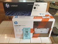 HP LaserJet M110we printer box stacked below HP 141A toner cartridge box with Maxsold lot tag.