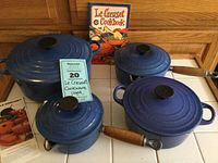 All four pots with lids and cookbook arranged on tiled countertop