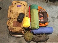 Photo showing the entire camping lot including Jansport backpack, rolled mats, tent bag, and fishing pouch arranged on carpet.