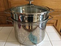 Front view of large stainless steel pot with steamer insert and glass lid on top.