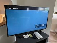 Sony Bravia TV powered on, showing HDMI 1 ARC input screen with included remote and manual on stand.