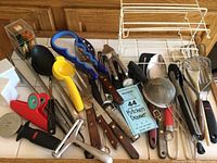 Photo showing all kitchen utensils and tools spread out on a surface including tongs, ladle, citrus juicer, grater, knives, clips, scissors, and wire rack.