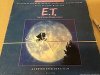 Front cover of the E.T. soundtrack cassette boxset showing bicycle silhouette flying across the moon, title text, credits: narrated by Michael Jackson, produced by Quincy Jones, music by John Williams.