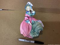 Full front and side view of the Royal Doulton porcelain figurine "Spring Morning" showing figure of a woman in pink dress and bonnet.