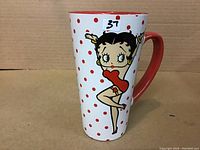 Tall white porcelain mug with red polka dots and a Betty Boop image in a red dress. Red interior and handle visible.